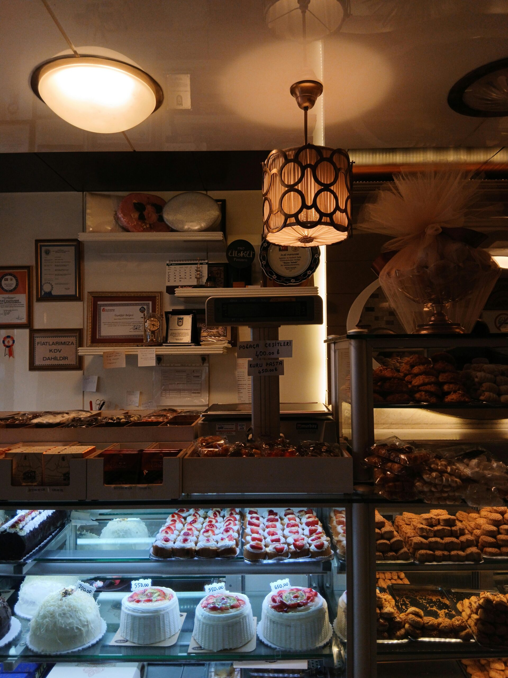 Warm bakery interior showcasing a variety of cakes and pastries on display shelves.