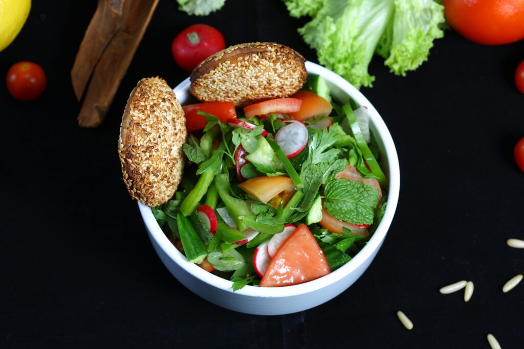 Colorful bowl of fresh vegetable salad with mint and sesame-topped bread, perfect for a healthy meal.